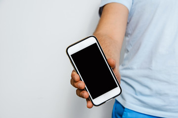 Phone in hand with a blank screen. A man wearing a white T-shirt is holding a phone with a blank display. Content completion concept.