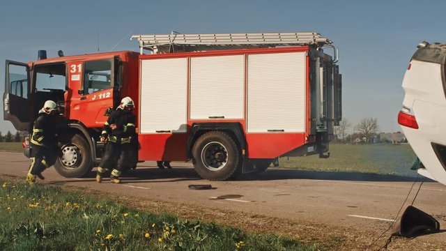 Rescue Team of Firefighters Arrive on the Car Crash Traffic Accident Scene on their Fire Engine. Firemen Grab their Tools, Equipment and Gear from Fire Truck, Rush to Help Injured People. Slow Motion