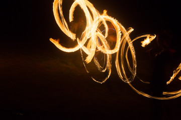 The artist shows a fire show at night spinning torches, circles of fire and loops