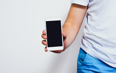 Phone in hand with a blank screen. A man wearing a white T-shirt is holding a phone with a blank display. Content completion concept.