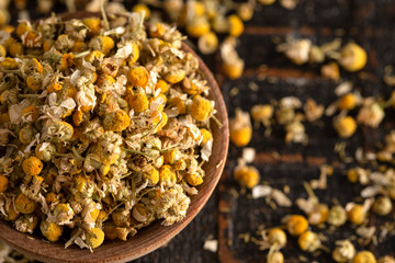 A Bowl of Dried Chamomile Flowers Spilled on a Dark Wooden Table