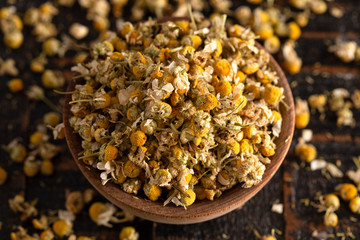 A Bowl of Dried Chamomile Flowers Spilled on a Dark Wooden Table