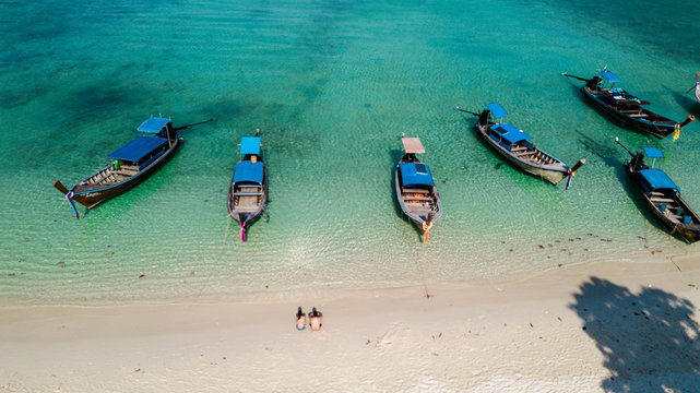 Couple on the sand of a tropical beach with longtail boats in Thailand. Crystal clear water. Drone view