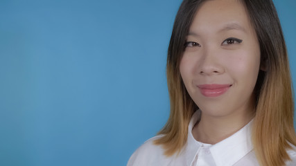 cheerful asian woman with blonde hair looking to the camera close up face on blue background in studio.
