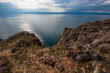 The rocky shore of Lake Baikal with mountains on the horizon. Steep cliff into the water.