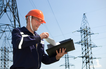 Electrician looking working drawings on the background of electric pylons - 277434919
