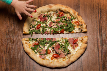child hand take one half of pizza with arugula and ham