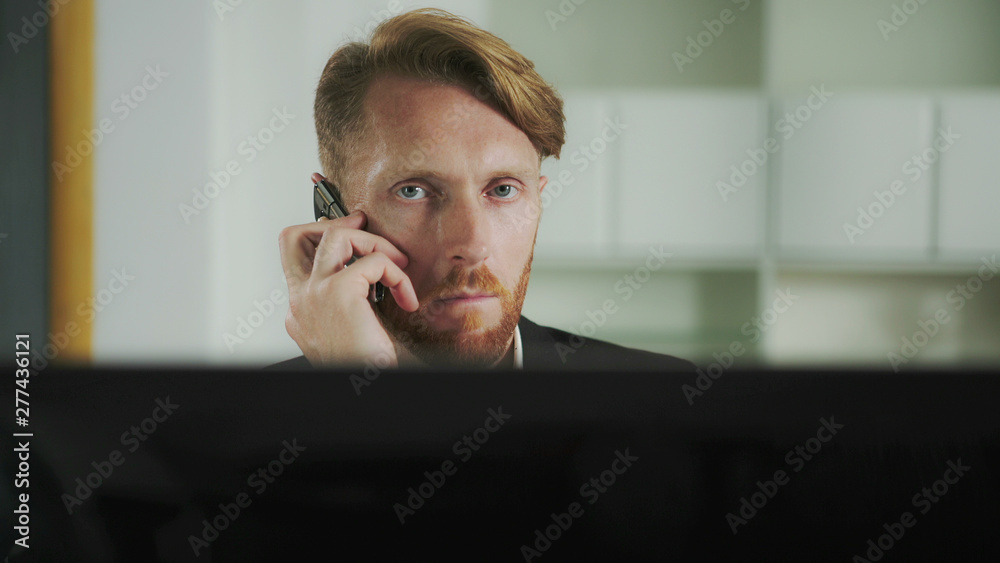 Poster Red-haired man sitting at a computer and calling on the phone. UHD