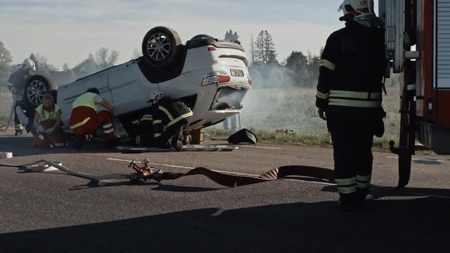 Rescue Team of Firefighters and Paramedics Work on a Terrible Car Crash Traffic Accident Scene. Preparing Equipment, Stretches, First Aid. Saving Injured and Trapped People from the Burning Vehicle