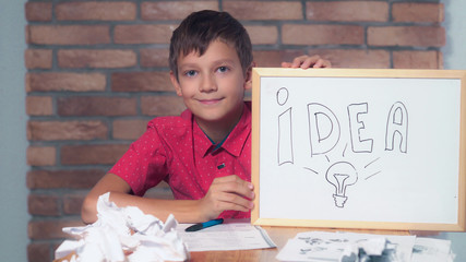 Portrait little boy showing whiteboard with handwriting idea. Child is lost in thought. Preadolescent wearing in casual red shirt. Schoolboy with happy friendly smile.