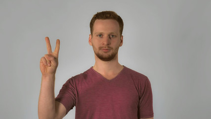 portrait happy young caucasian man on grey background chinese number gestures. caucasian guy with red hair make a gesture with the hand shows the countdown from five to start. handsome redhead men