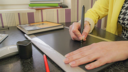 A girl in a yellow jacket draws on the tablet. At work