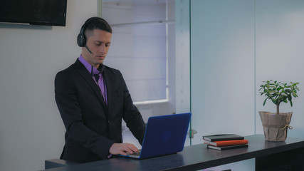 Portrait man receptionist standing at service desk talking with client entering data on computer....