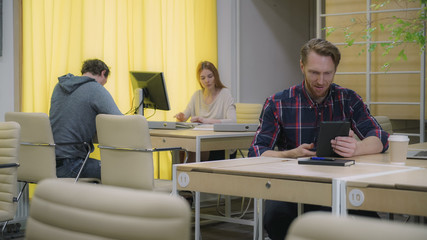 A bearded man talking on a tablet in the eco office workers work