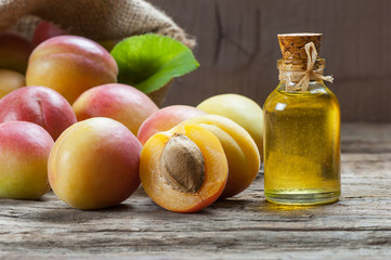 Glass bottle of Apricot seed kernel oil ( prunus armeniaca oleum ) with fresh ripe apricot fruits on wooden rustic background