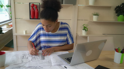 mixed race worker in architectural agency working with sketch holding pencil and ruler. Young professional woman sitting at the desk.