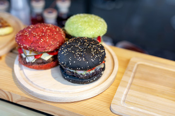 Three tasty bright multicolored beef burgers on wooden counter at food fest. amburger bun clolred with tomato, basil and cuttlefish ink