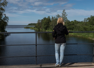 Fototapeta premium A girl stands on a bridge and looks into the distance. The river flows into the lake. Spring. Sunny day.