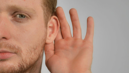 Obraz premium close up part of face young man with beard red hair posing showing hand gesture puts his hands to ear and listening