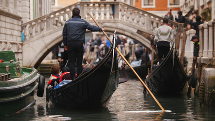 Fototapeta na wymiar A man stands on a boat with people holding a paddle in his hand - Journey about the canals of Venice