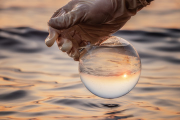 Analysis of the water in the lake. In the hand of a laboratory sample of water from the reservoir. In a glass bulb can be seen the setting sun
