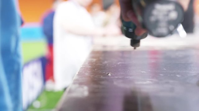 Close-up of worker's hand drilling tightening the screw to the wooden table at the stadium. Action. World Cup 2018 in Russia
