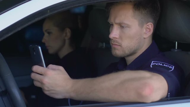 Policeman monitoring emergency calls in phone while sitting with partner in car