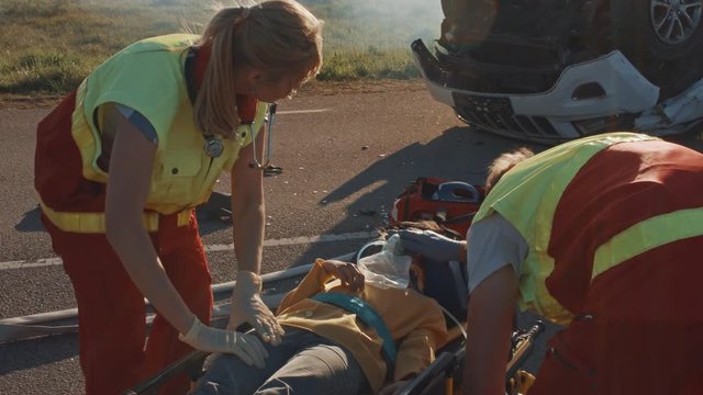 On the Car Crash Traffic Accident Scene: Paramedics Saving Life of a Little Girl Lying on Stretchers, She’s given Best First Aid Help. Professional Medics Doing their Job Best