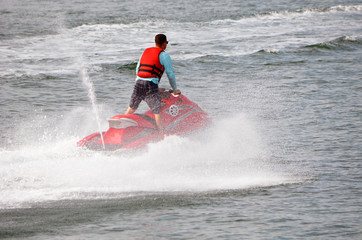 Young man standing up on a speeding red jet ski