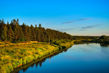 Summer landscape river with reflecting trees against the backdrop of forests and mountains.