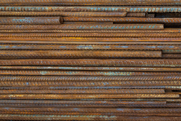 Top view stack of straight old rusty high yield stress deformed reinforcement steel or iron bars. Background horizontal random pattern of deformed iron bars. 