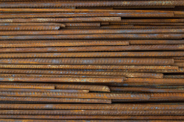 Top view stack of straight old rusty high yield stress deformed reinforcement steel or iron bars. Background horizontal random pattern of deformed iron bars. 