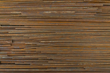 Top view stack of straight old rusty high yield stress deformed reinforcement steel or iron bars. Background horizontal random pattern of deformed iron bars. 