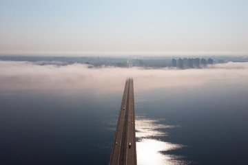 Fog or mist over river bridge with car traffic in city, aerial panoramic view