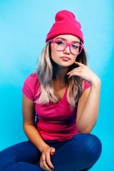 Naklejka premium young pretty teenage modern hipster girl posing emotional happy on blue background, lifestyle people concept