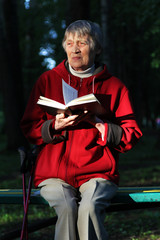 An elderly woman is resting after a walk on a park bench. Reading book, thinking. Watching the sunset.