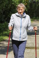 Portrait of Elderly woman (80 y.o) who is engaged in Nordic walking. Doing sport in the park in sunlight.