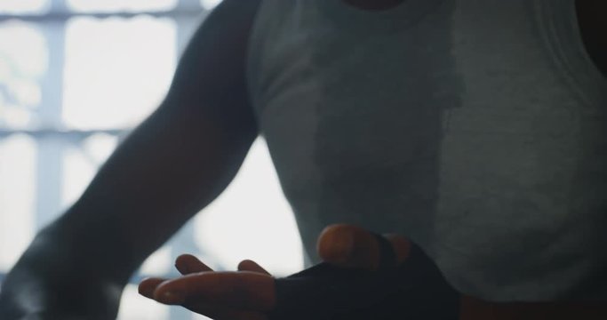Cinematic slow motion shot of a professional young muscular african man is wrapping black bandages before to start practicing shadow boxing work out in a ring. 