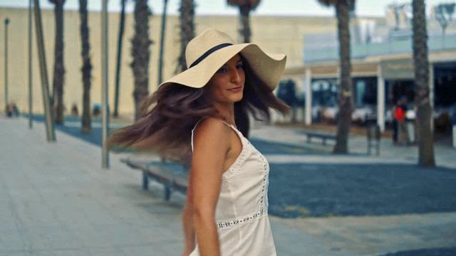 Pretty woman wearing white dress and pamela hat walking over the beach terrace at sea. Happy summer vacation