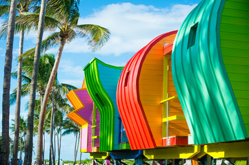 Fototapeta premium Bright scenic view of colorful new lifeguard towers standing in a row with the shadows of palm trees in South Beach, Miami, Florida, USA