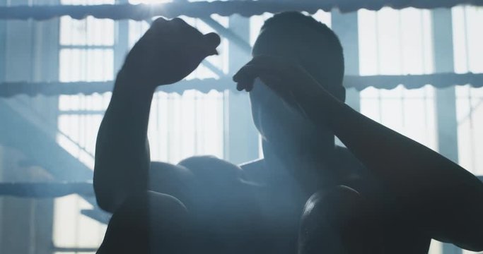 Cinematic slow motion shot of a professional young muscular shirtless african man is practicing shadow boxing work out in a ring. 