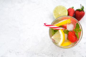 Glass of refreshing drink on white stone table. Top view, copy space. Sweet water with strawberry, mint, lime and lemon.