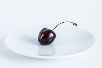 Burgundy cherry berry on a white plate close-up on a white background