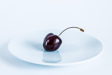 Burgundy cherry berry on a white plate close-up on a white background