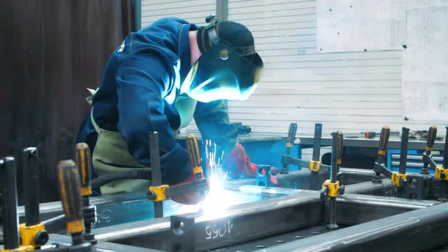 Professional welder in protective uniform with face mask welding with electrode