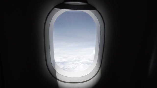 Slow motion dolly out or pullout of a plane window in the cabin with amazing blue sky and white clouds