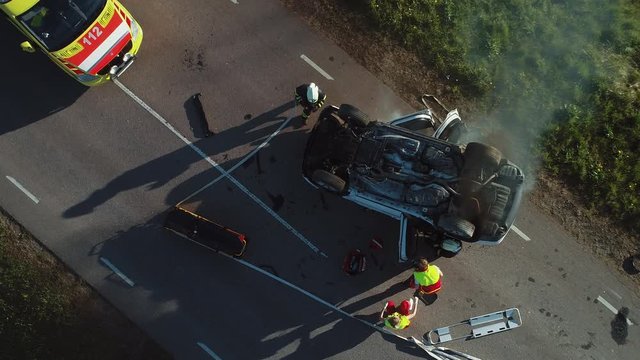 Aerial View: Rescue Team of Firefighters and Paramedics Work on a Car Crash Traffic Accident Scene. Preparing Equipment, First Aid Help. Saving Injured and Trapped People from the Vehicle. Zoom in
