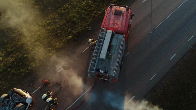 Aerial View: Rescue Team of Firefighters and Paramedics Work on a Car Crash Traffic Accident Scene. Preparing Equipment, First Aid Help. Saving Injured and Trapped People from the Burning Vehicle