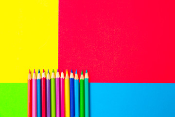 Colorful background with many pencils crayons pastels lined up on multi color backdrop - Top view...