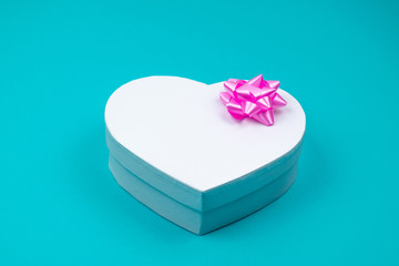 White heart shaped gift box with pink bow for holiday, christmas, thanks giving day, birthday top view isolated on blue background. 
